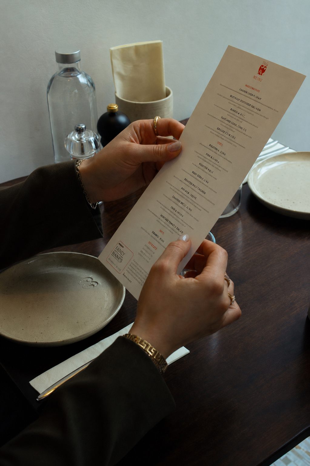 Two hands holding a tall printed restaurant menu at a set table.